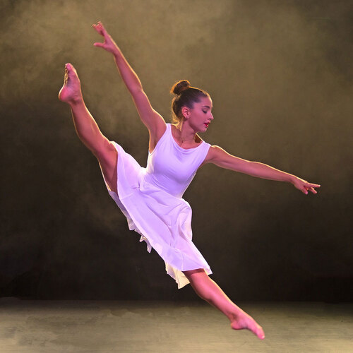 Eine Ballettänzerin tanzt im Bühnenlicht in einem weissen Kleid